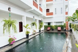 Un hôtel à plusieurs étages doté d’une piscine centrale, de plantes en pot et d’un espace extérieur aménagé pour s’asseoir.
