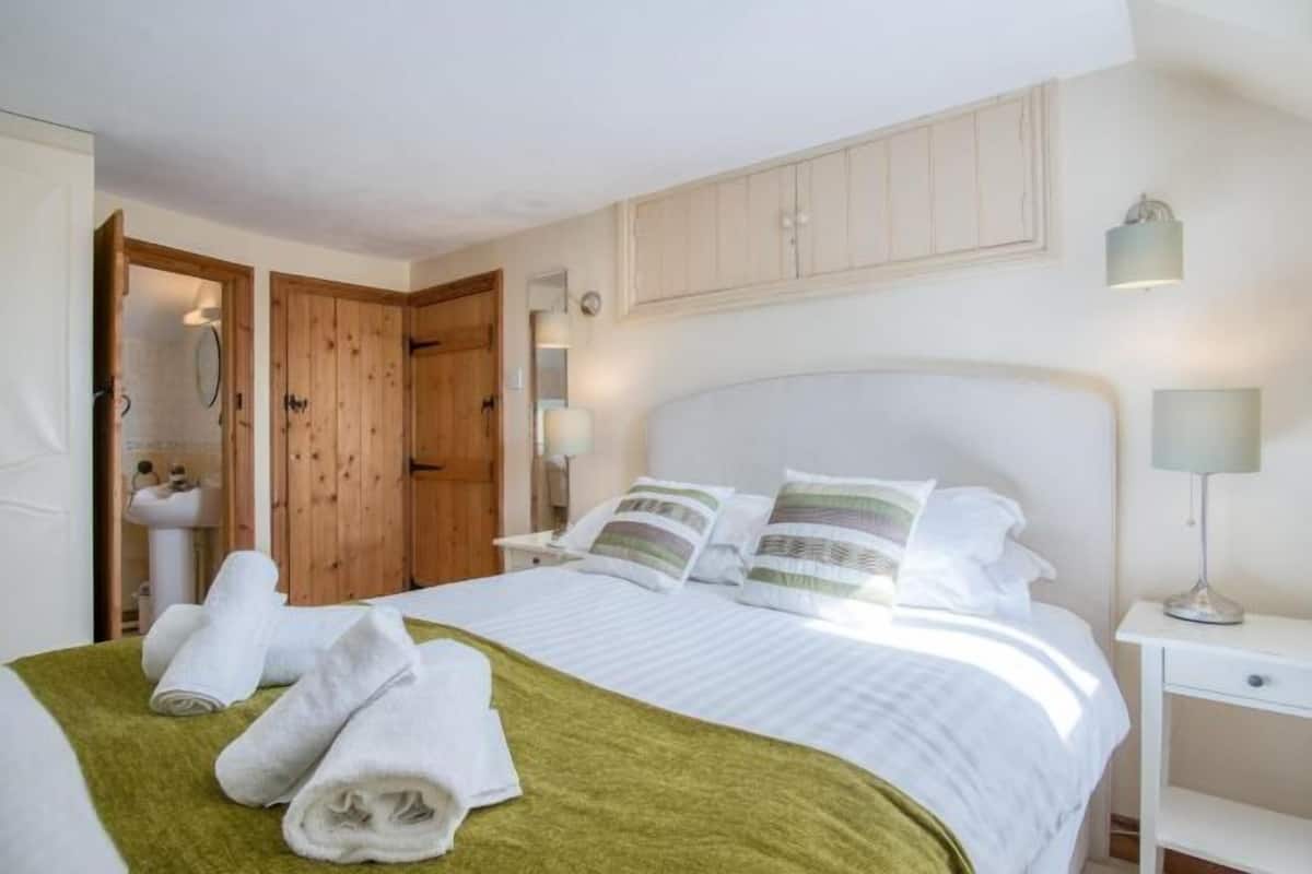 A bedroom with a bed, pillows, a bedside table, a lamp, and a wooden door.