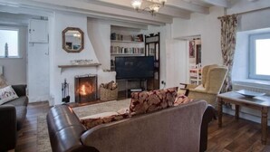 Una sala de estar con chimenea, televisor, estantería y una silla.