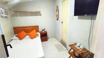 A bedroom with a bed, a wooden nightstand, a television mounted on the wall, and a small table with cups.