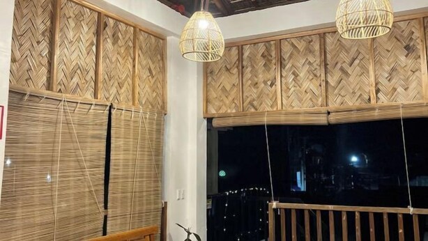 A room with bamboo panel walls, two hanging light fixtures, and a view through a large window. - Sunny Terrace (Baler)