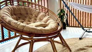 A wicker chair with a cushioned seat and backrest, positioned on a balcony with a view of the outdoors. - Sunny Terrace (Baler)