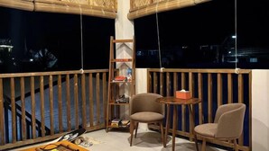 A balcony with wooden railings, a small table, two chairs, a shelf with books and a toy, and a view of the night sky. - Sunny Terrace (Baler)