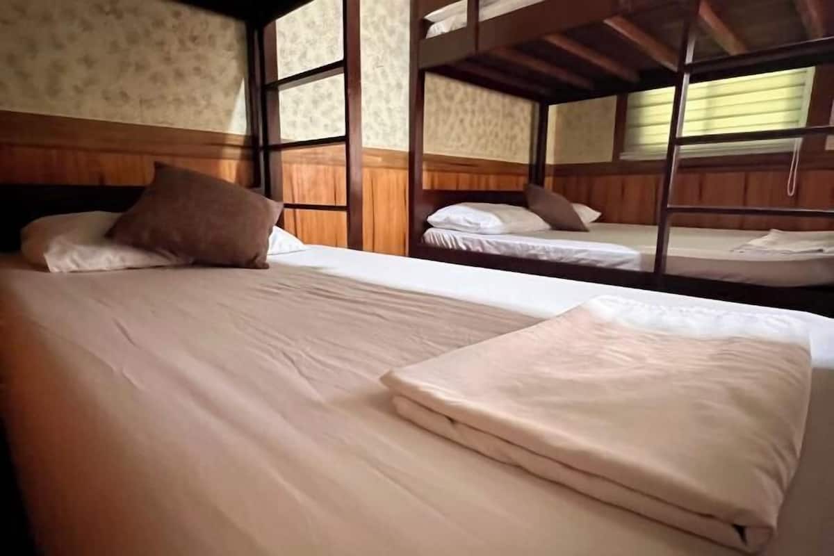 A room with bunk beds, wooden walls, and a window with blinds.