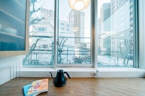 A room with a large window, a black kettle, and a bag of snacks on the floor.