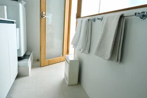 A bathroom with a shower, a toilet, and a towel rack with towels.