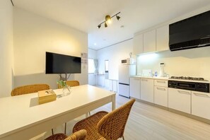 A modern kitchen with white cabinets, a flat-screen TV, wicker chairs, and a dining table. - Akisapo Stay Motohasunuma (Tokyo)