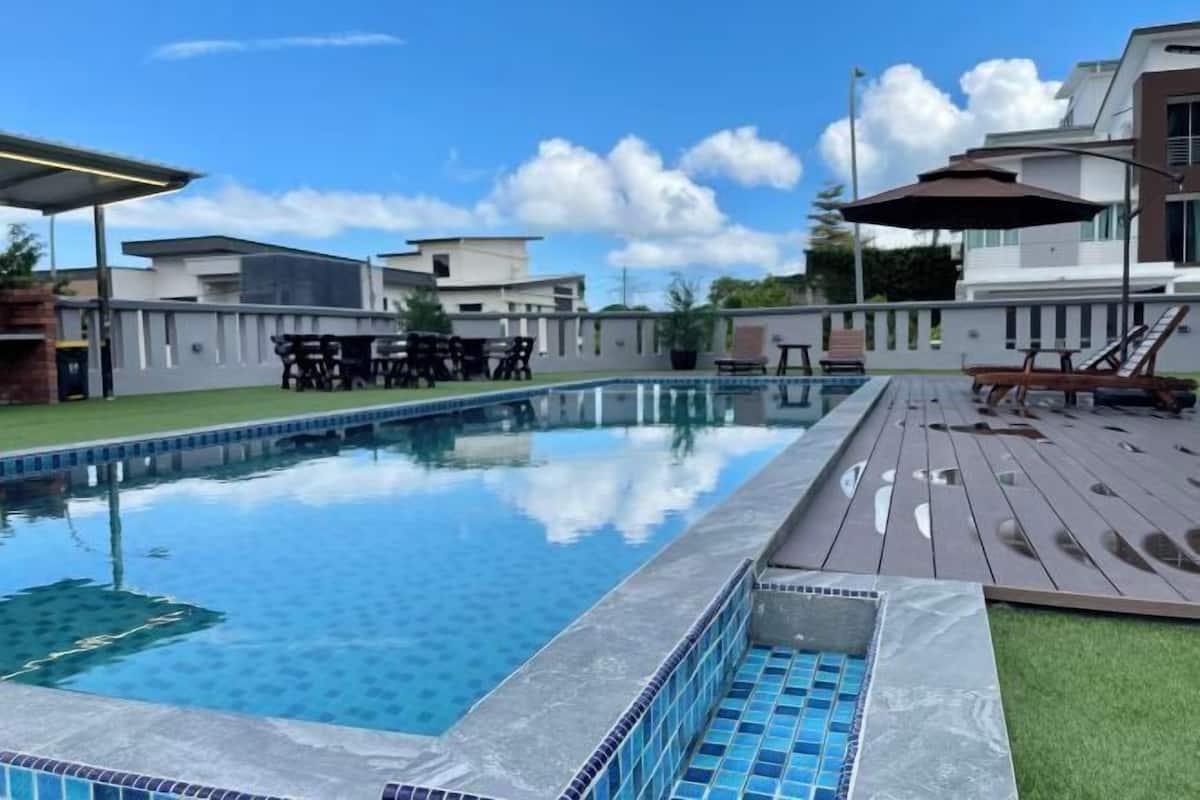 A swimming pool with a tiled edge, surrounded by a deck with lounge chairs and a table.