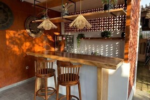 A bar area with a wooden counter, two stools, hanging wicker lamps, and a decorative lattice wall. - Munay Villa (Bali)