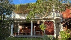 A two-story building with a covered porch, a brick wall, and a garden with a tree and potted plants. - Munay Villa (Bali)