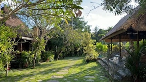 A garden with a thatched-roof structure, stone pathway, and lush greenery. - Munay Villa (Bali)