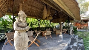 A covered outdoor seating area with stone statues, wicker furniture, and a thatched roof. - Munay Villa (Bali)