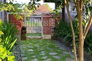 A garden pathway with stepping stones leading to a gate with a red lattice design. - Munay Villa (Bali)