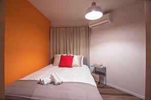 Una habitación de hotel con cama, aire acondicionado, mesita de noche y ventana con cortinas.