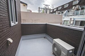 Una terraza en la azotea con un muro de ladrillo, una ventana y una unidad de aire acondicionado blanca.