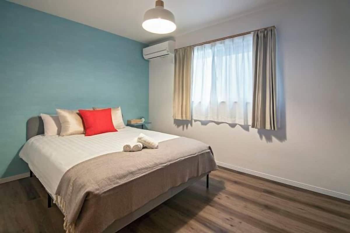 A bedroom with a bed, a nightstand, a window with curtains, and an air conditioning unit.