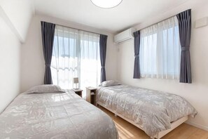 Une chambre avec deux lits, une table de chevet, une fenêtre avec des rideaux et un appareil de climatisation.