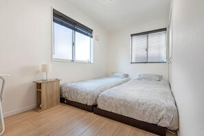 Une chambre avec deux lits, une table de chevet avec une lampe et une fenêtre avec des stores.