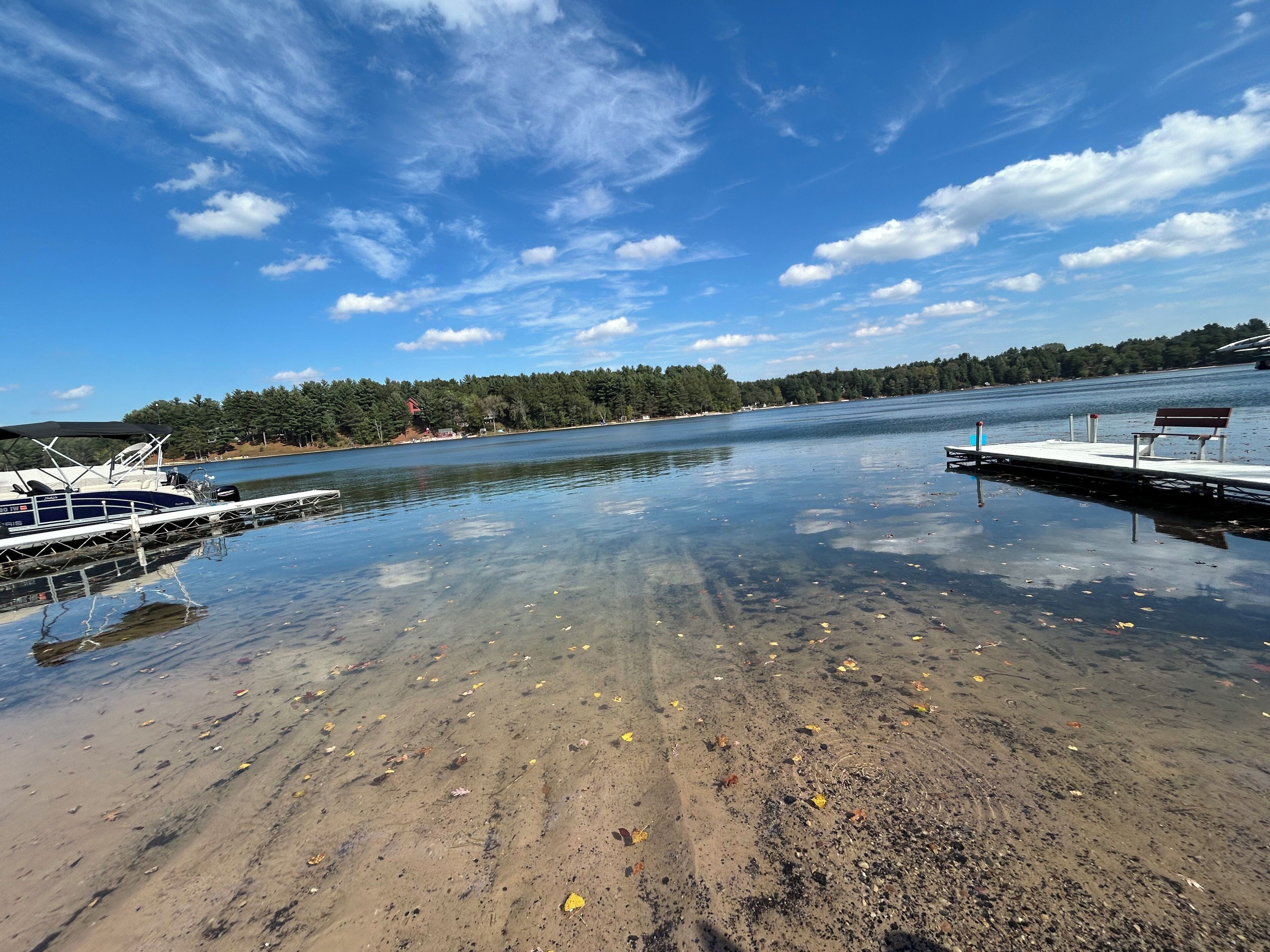 A calm lake with a dock and a boat, surrounded by trees and a clear sky.