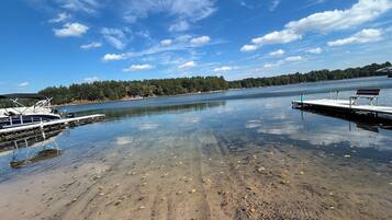 A calm lake with a dock and a boat, surrounded by trees and a clear sky.