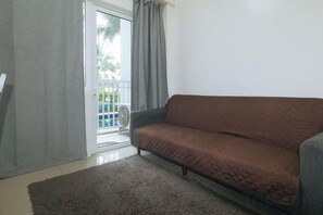 A living room with a sofa, a door leading to a balcony, and a fan. - Lascianos SMDC Shore Residences by RedDoorz (Pasay)