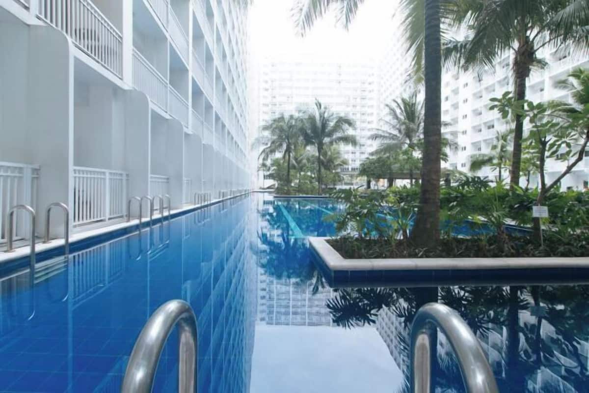 A swimming pool with metal railings, surrounded by palm trees and a high-rise building in the background.