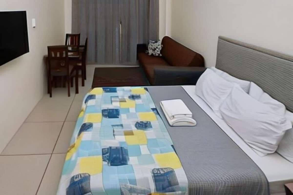 A hotel room with a bed, a sofa, a TV, and a dining area with chairs and a table.