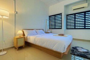 Een slaapkamer met een bed, bedlampje, ramen en een airconditioning.