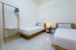 A room with two single beds, a wooden bed frame, a metal drying rack, and a bedside table with a lamp. - Wawasan Puchong Family-Friendly Spacious Home (Puchong)