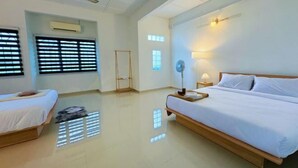 Ein Hotelzimmer mit einem Bett, zwei Nachttischen, einem Standventilator, einem Deckenventilator und einem Fenster mit Jalousien.