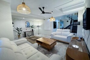 A modern living room with a white sofa, a wooden coffee table, and a ceiling fan. - Wawasan Puchong Family-Friendly Spacious Home (Puchong)