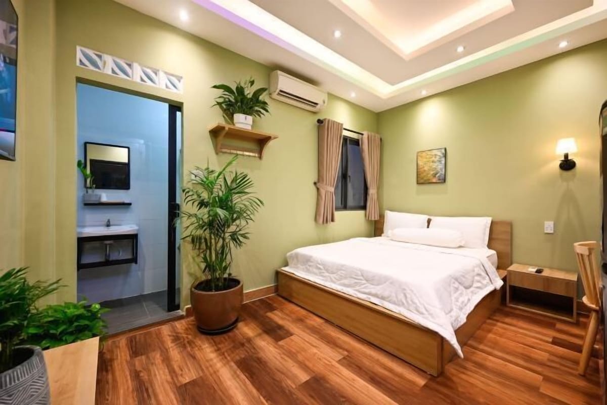 A bedroom with a wooden bed, a potted plant, a wall-mounted air conditioner, and a small bedside table.