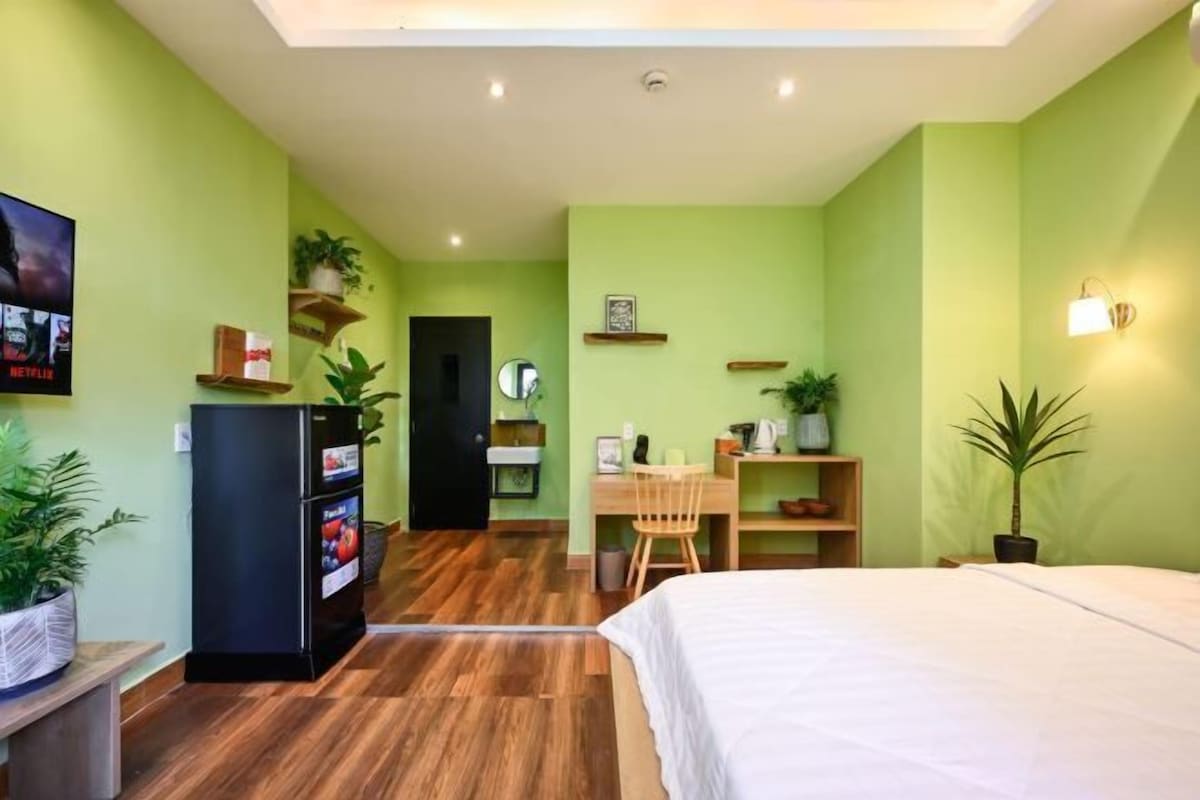 A compact hotel room with a bed, a desk with a chair, a refrigerator, and a TV on the wall.