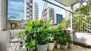 A balcony with potted plants, a metal railing, and a view of tall buildings. - Elegant Feel Inn - M&A (Ho Chi Minh City)