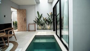 A modern indoor pool area with a wooden bench, a small table, and potted plants. - The Eight Bali Seminyak (Bali)
