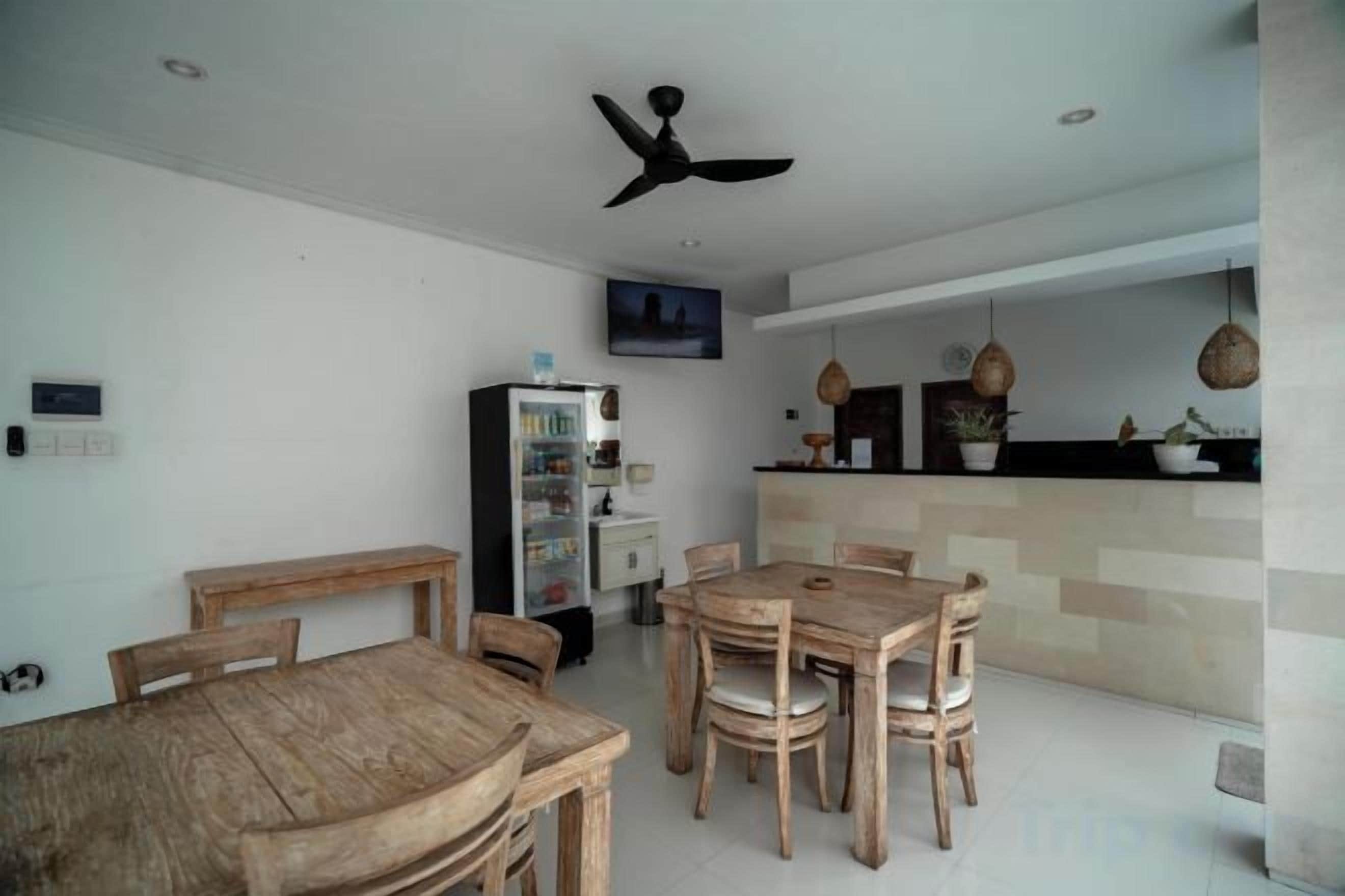 A dining area with a wooden table and chairs, a ceiling fan, a refrigerator, and a kitchen counter with plants.
