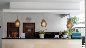 A reception area with a counter, hanging wicker lamps, a wooden door, and potted plants. - The Eight Bali Seminyak (Bali)
