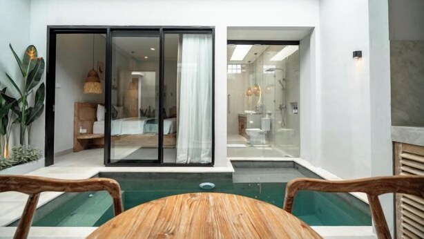 A modern hotel room with a glass door leading to a bathroom, a small pool area, and a wooden table. - The Eight Bali Seminyak (Bali)