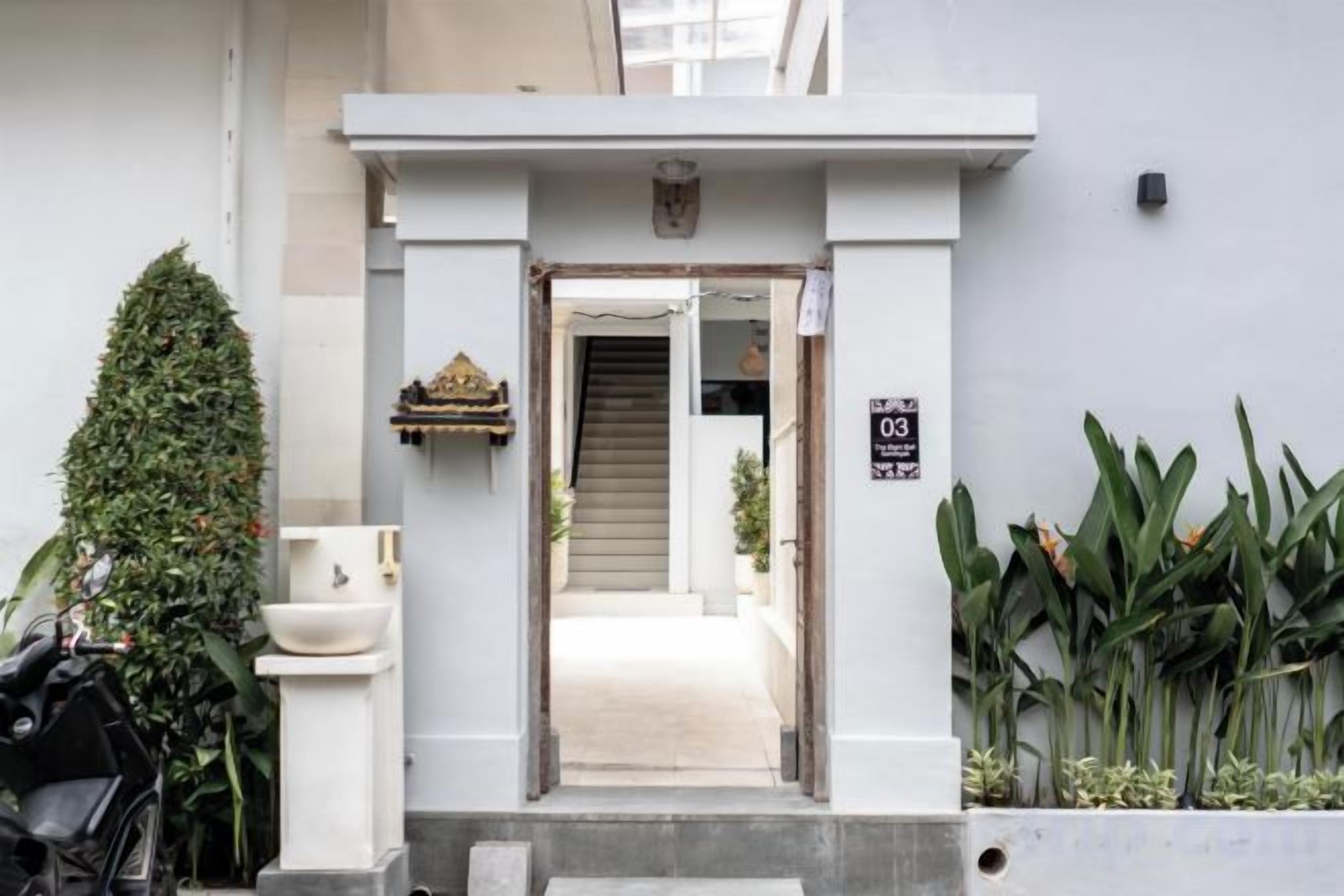 A hotel entrance with a white facade, a sign indicating room number 03, and a staircase leading to the interior.