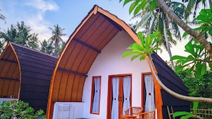 A small, single-story house with a sloped roof, a porch with a chair, and a small table. - Nusa Pelangi Bungalow (Penida Island)