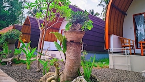 A tropical garden with potted plants and a small tree, surrounded by a building with a curved roof and a balcony. - Nusa Pelangi Bungalow (Penida Island)
