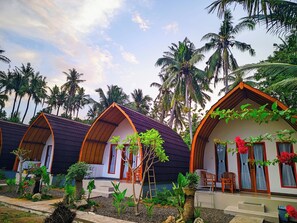A row of bungalow-style accommodations with curved roofs, surrounded by lush greenery and palm trees. - Nusa Pelangi Bungalow (Penida Island)