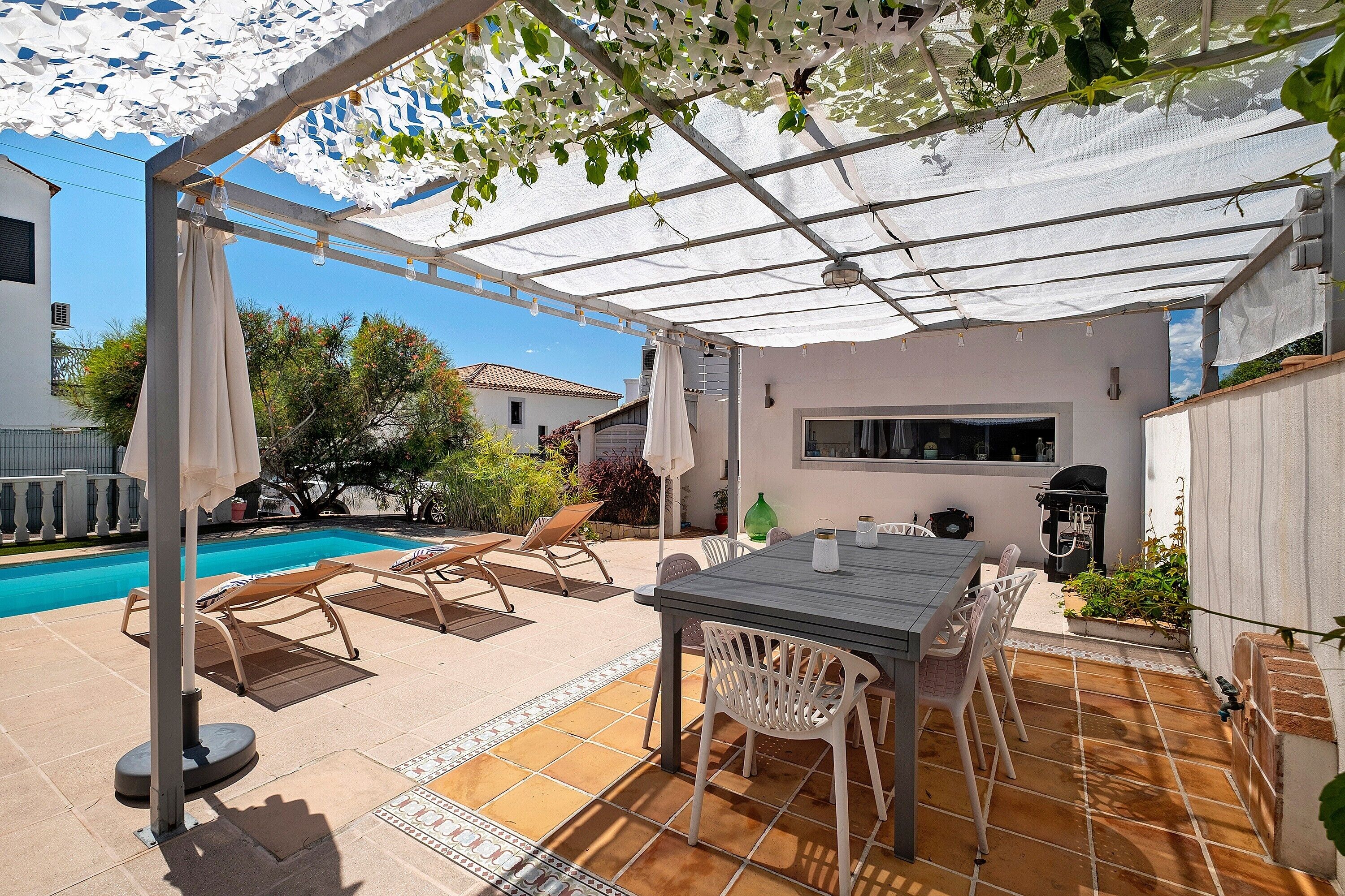 Un patio con tavolo e sedie, una piscina e un pergolato con tenda bianca.