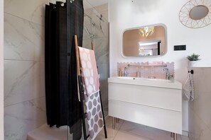 Un bagno con un mobile lavabo bianco, uno specchio con cornice geometrica e una doccia separata da un tendaggio nero.
