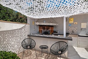 Un área de cocina al aire libre con una barra, dos sillas y un techo decorativo.