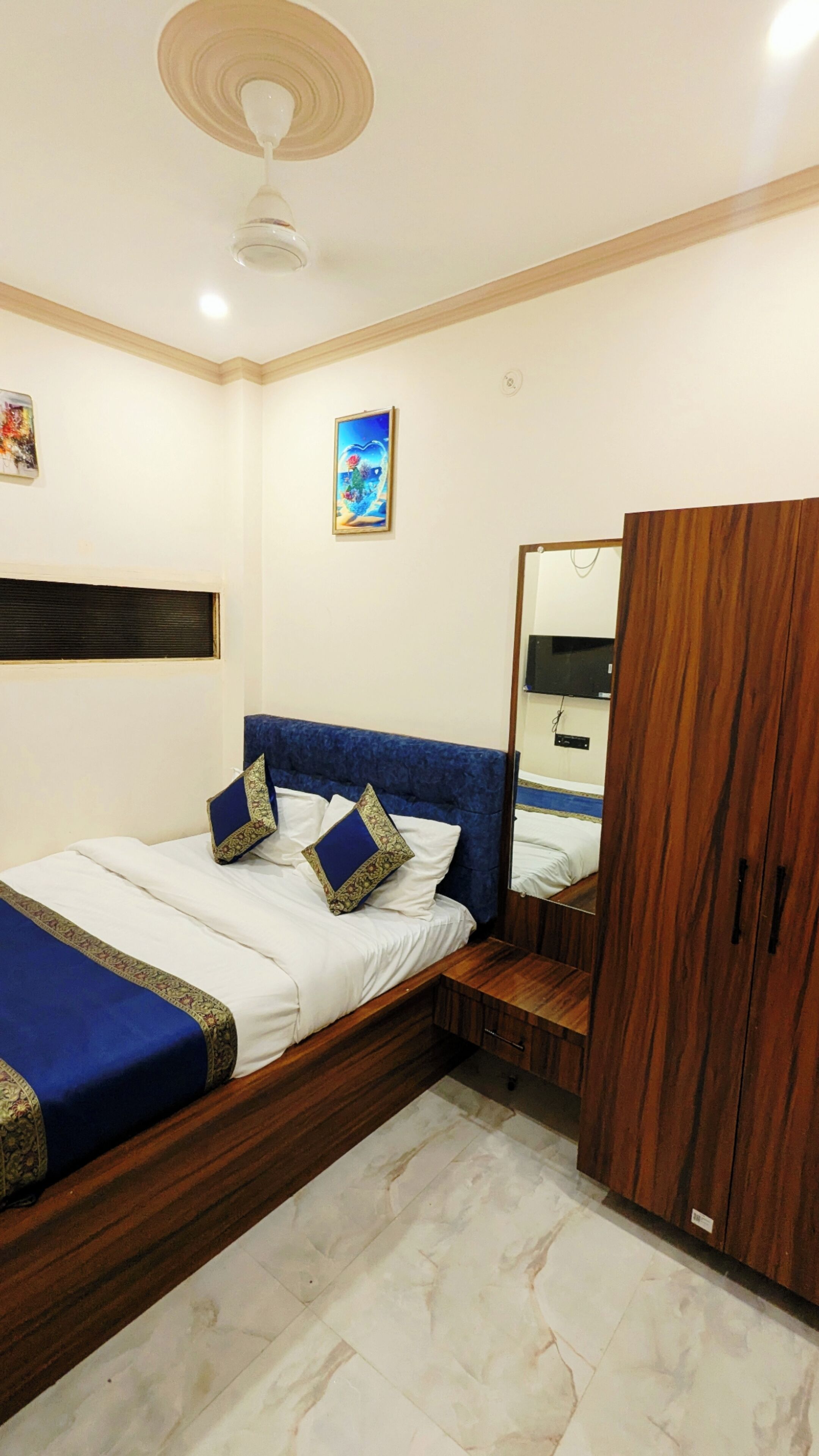 Une chambre à coucher comprenant un lit, une armoire, un ventilateur de plafond et un téléviseur fixé au mur.