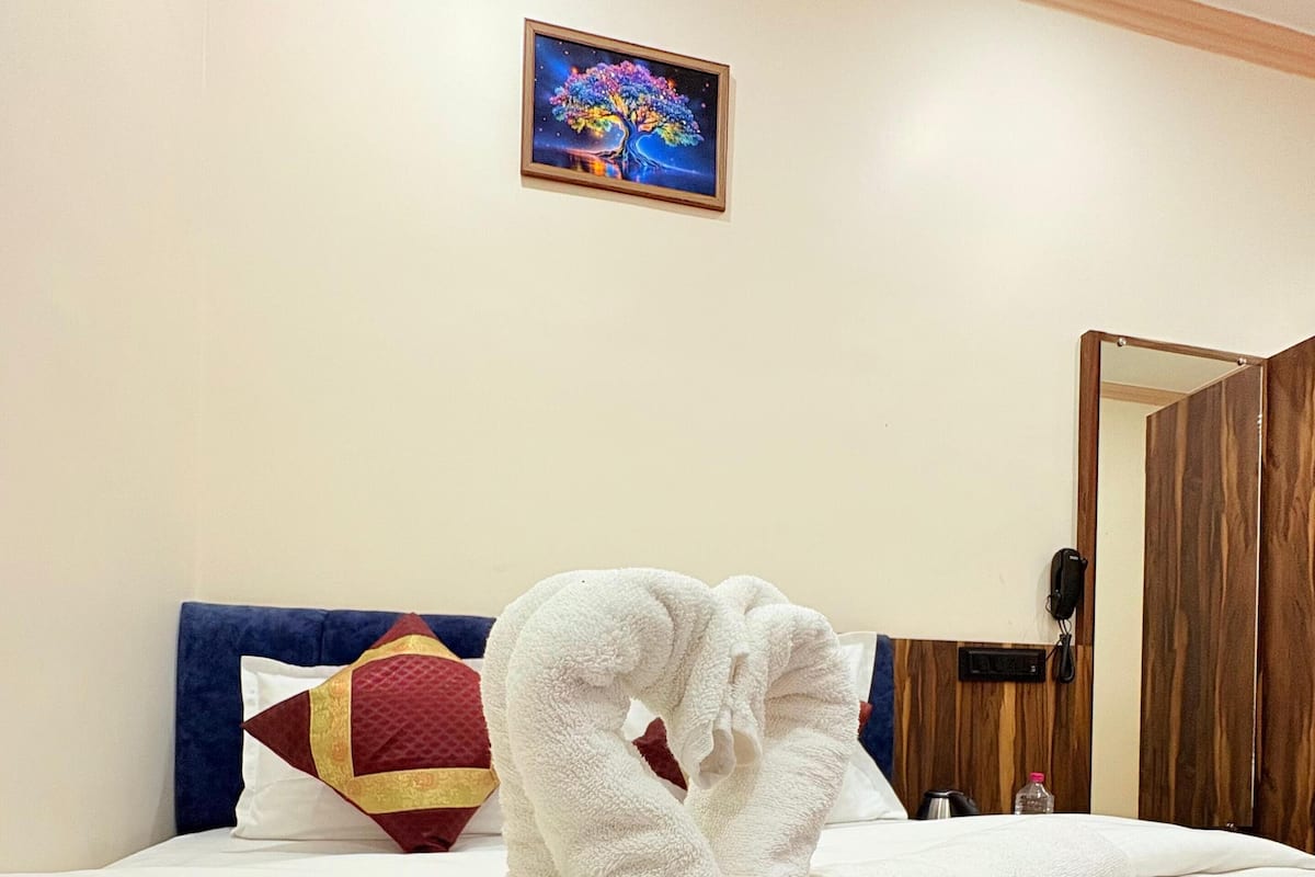 A hotel room with a neatly made bed, a red and white pillow, a framed artwork on the wall, and a wooden door.