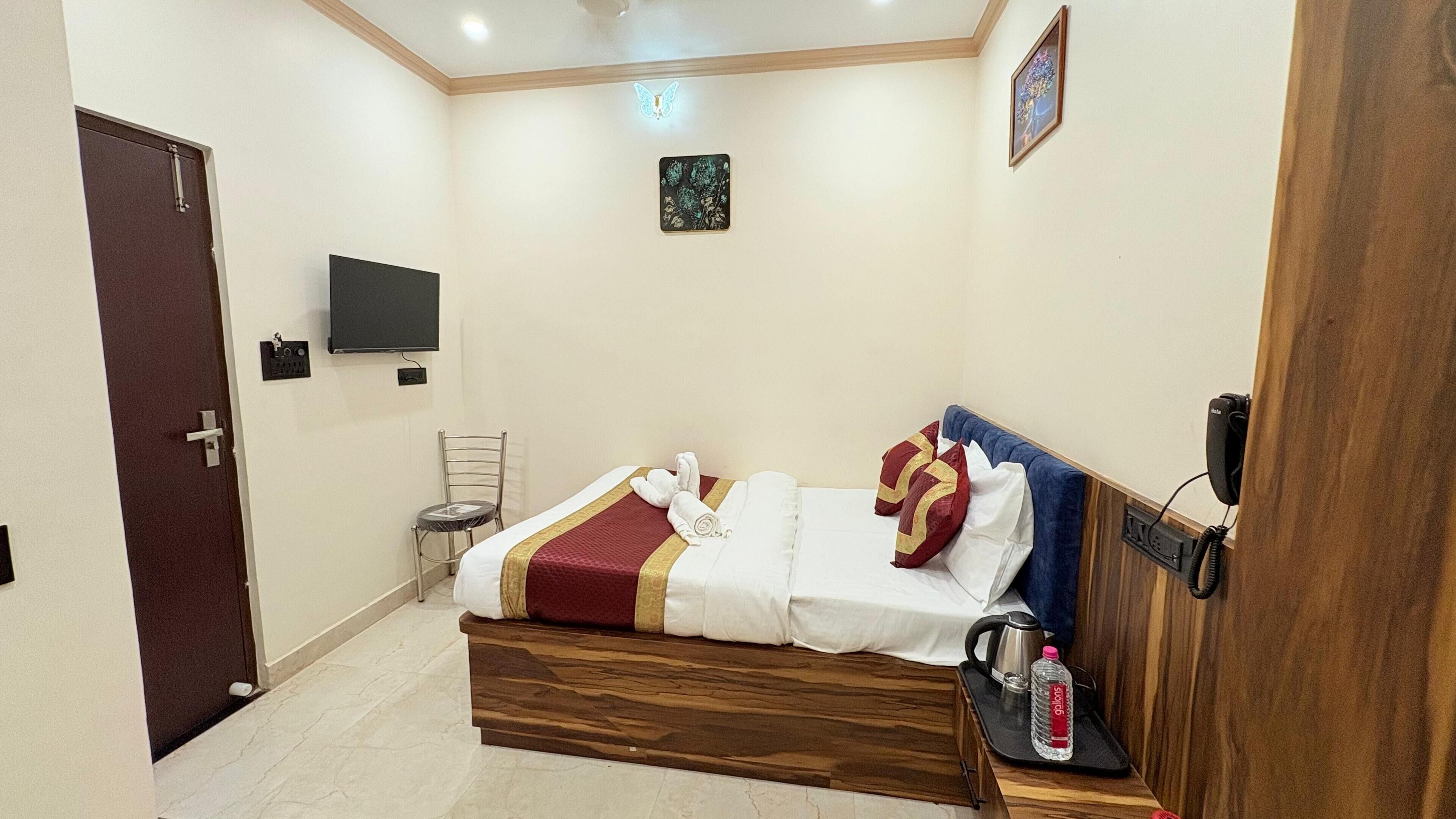Una habitación de hotel con una cama, una silla, un televisor, una lámpara de pared y una puerta.