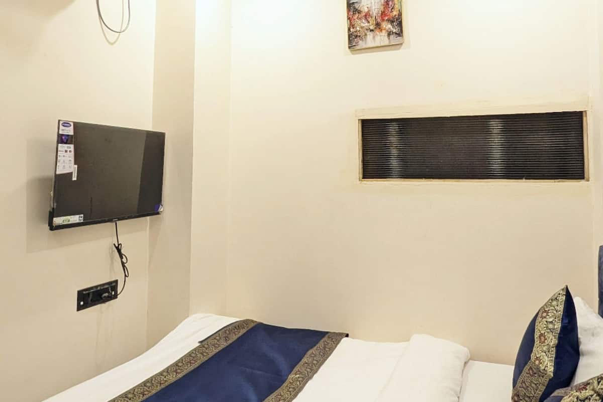 A hotel room with a bed, a flat-screen TV mounted on the wall, a ceiling fan, and a small artwork above the bed.