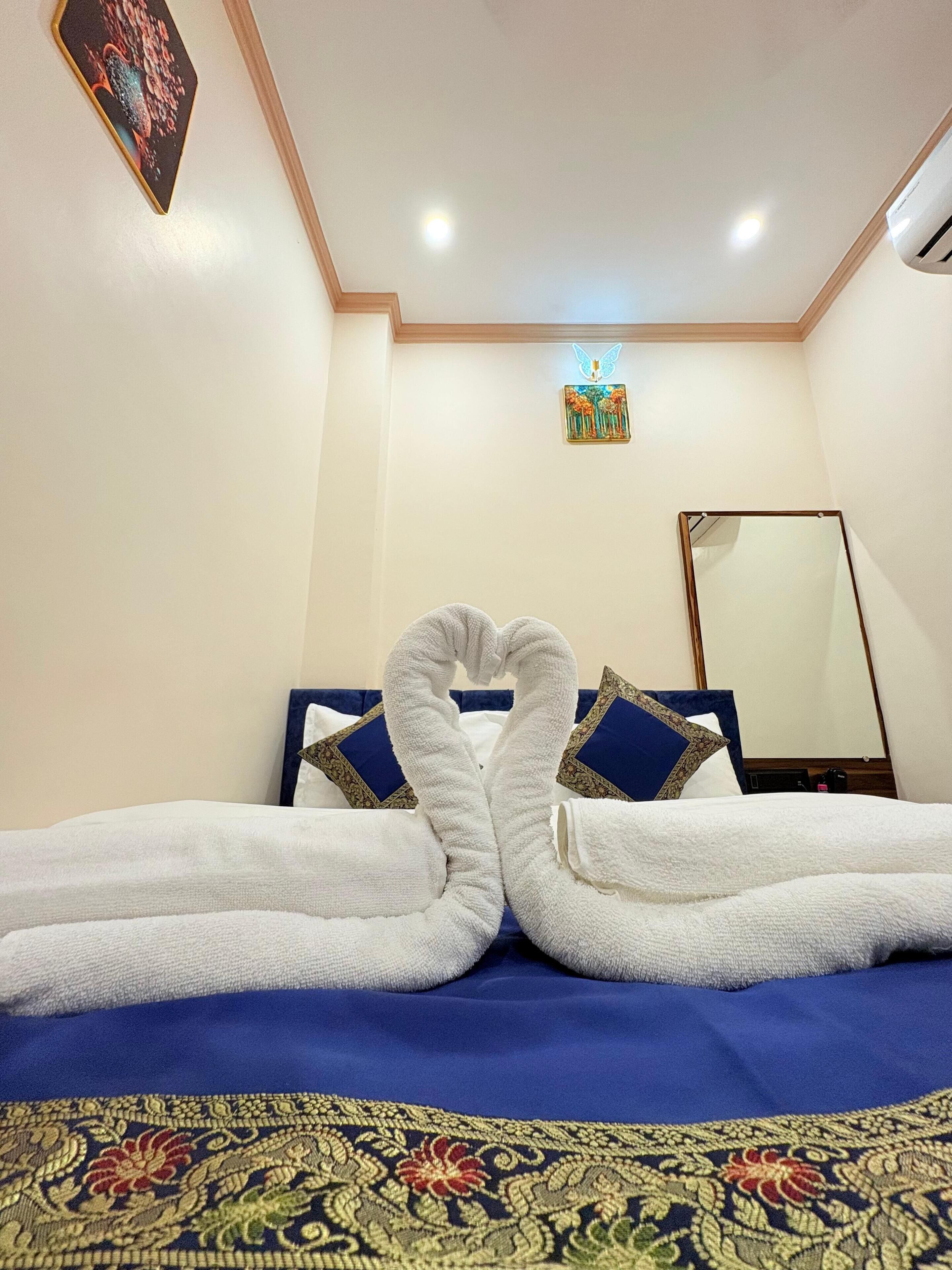 A hotel room with a neatly made bed, a decorative wall hanging, and a ceiling light.